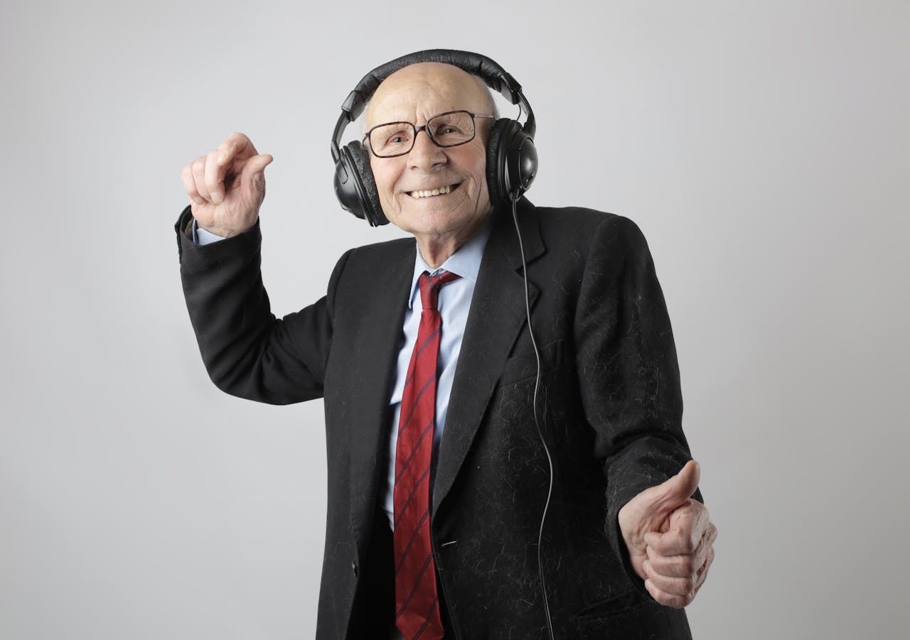 Happy senior man in formal attire delighting in music with headphones on a white background.
