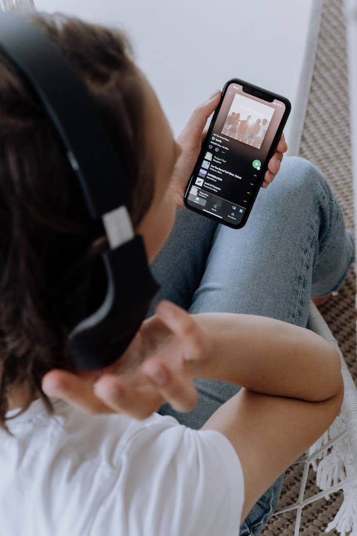 Person wearing headphones, using a smartphone to listen to music in a comfortable setting.
