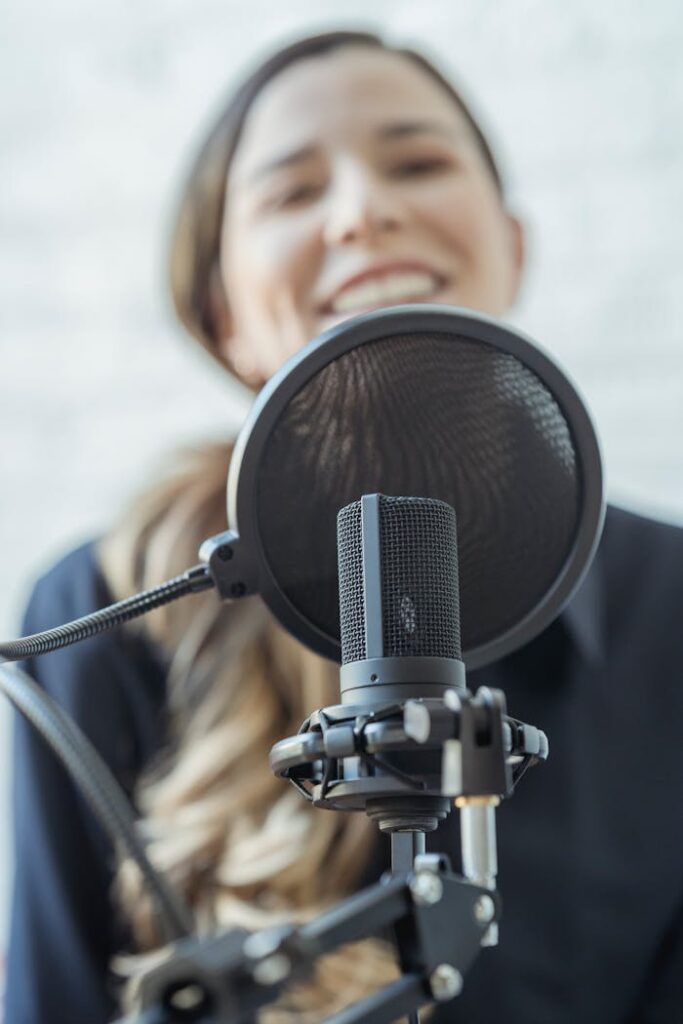 pexels photo 6953669 A woman smiles while recording with a professional microphone. Perfect for media and broadcasting themes.